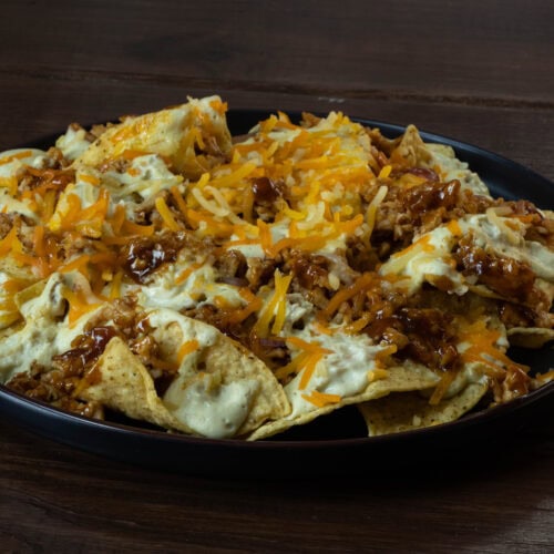 Plate of loaded nachos with shredded BBQ tofu, vegan cheese, and cashew queso.