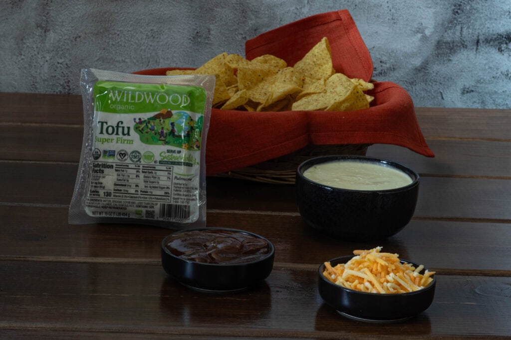 Ingredients for the BBQ Tofu nachos sitting on a table - super firm tofu, tortilla chips, bbq sauce, vegan cashew queso and vegan shredded cheese.