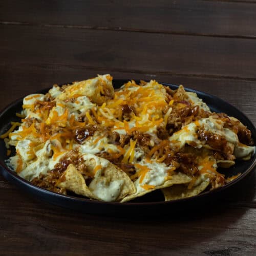 Plate of loaded nachos with shredded BBQ tofu, vegan cheese, and cashew queso.