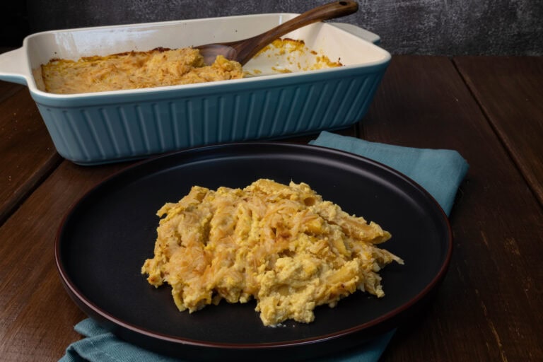 A plate of butternut squash pasta bake with a casserole dish with the remaining pasta in the background.