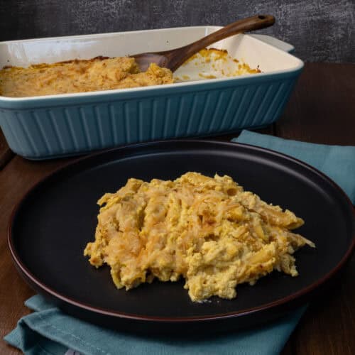 A plate of butternut squash pasta bake with a casserole dish with the remaining pasta in the background.