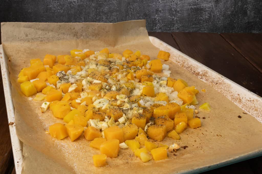 Oven roasted butternut squash, onion and garlic on a parchment paper lined baking sheet.
