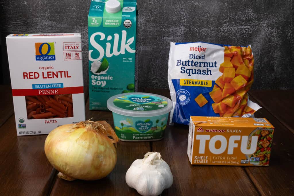 Ingredients on a table - red lentil penne pasta, soy m ilk, vegan paremsan, onion, garlic, silken tofu and butternut squash.