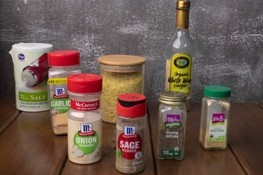 Ingredients sitting on a table - salt, garlic powder, onion powder, rubbed sage, nutritional yeast, thyme, white wine vinegar, and ground mustard.