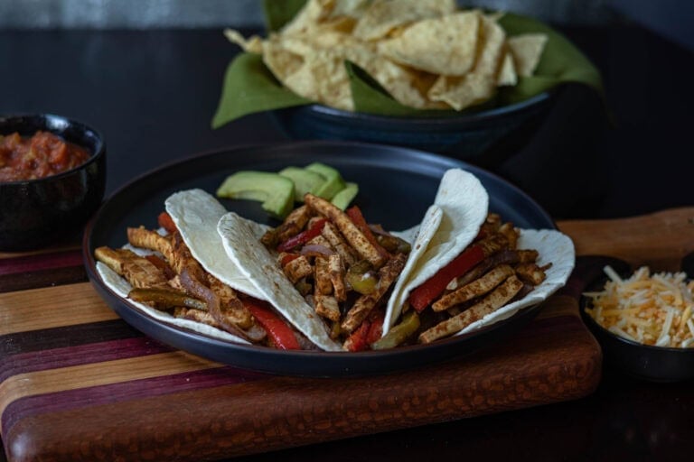Tofu fajitas on a black plate with tortilla chips in the background.