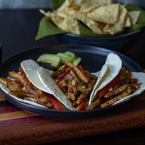 Tofu fajitas on a black plate with tortilla chips in the background.