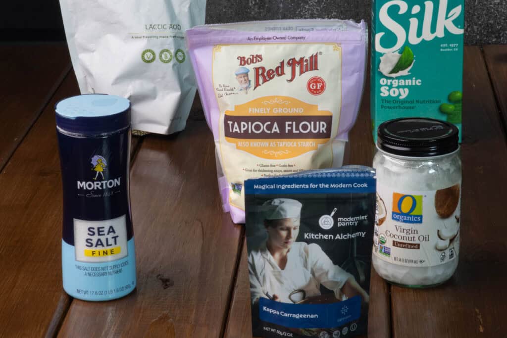Fresh mozzarella ingredients sitting on a table - lactic acid, tapioca flour, soy milk, coconut oil, kaapa carrageenan and sea salt.