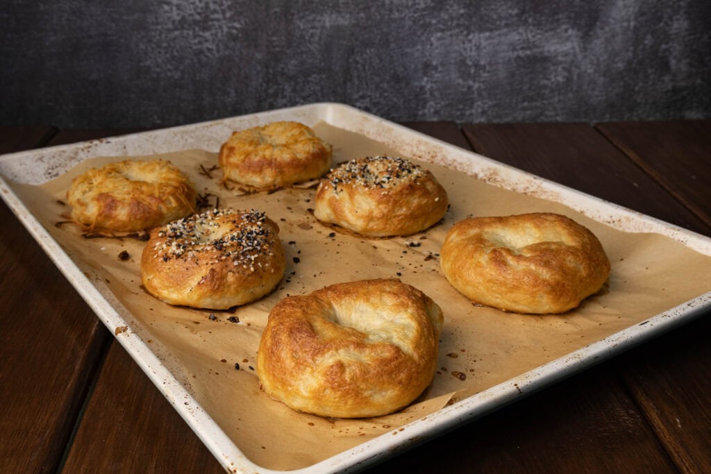 Baking sheet with three types of high protein bagels - toasted parmesan, everything and plain.