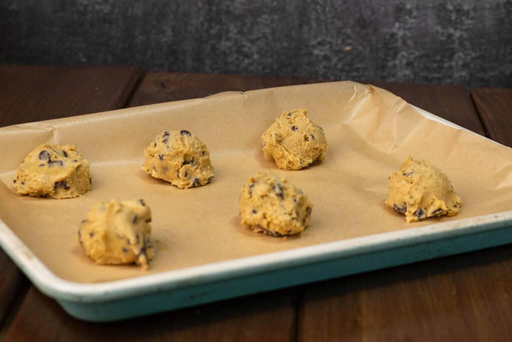 Uncooked pumpkin chocolate chip cookies on a parchment paper lined baking sheet.