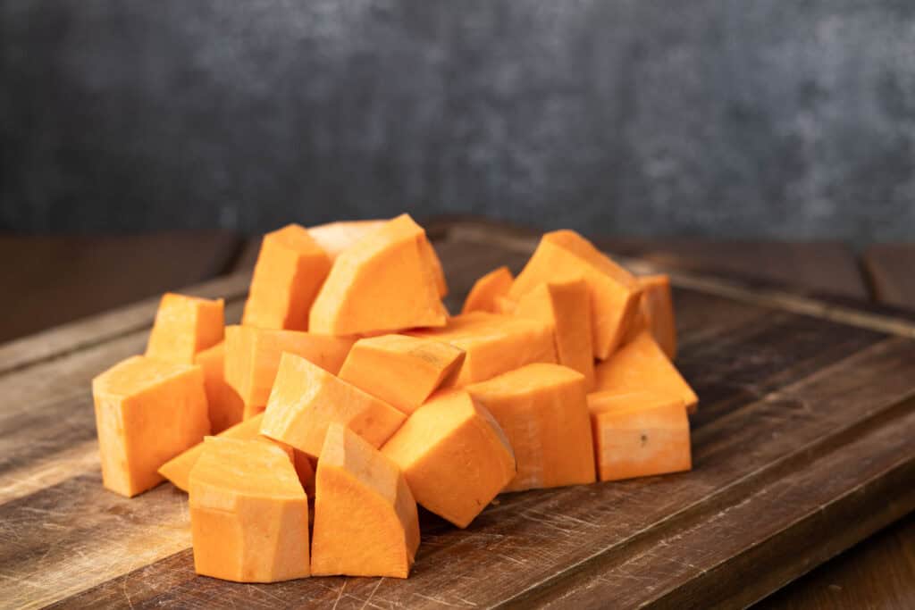 Sweet potato chunks on a wooden cutting board.