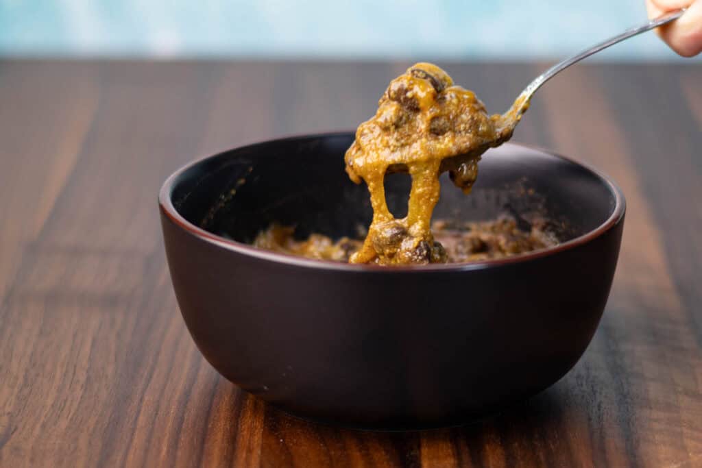 Vegan cheesy taco black beans in a black bowl on a wooden counter.