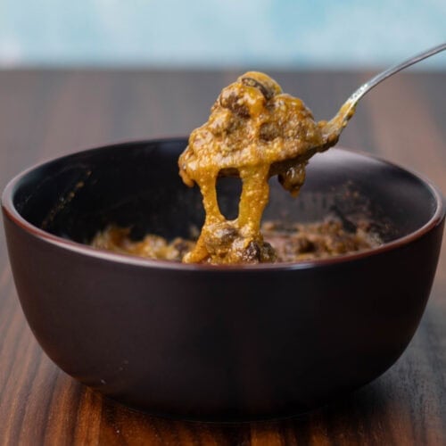Vegan cheesy taco black beans in a black bowl on a wooden counter.