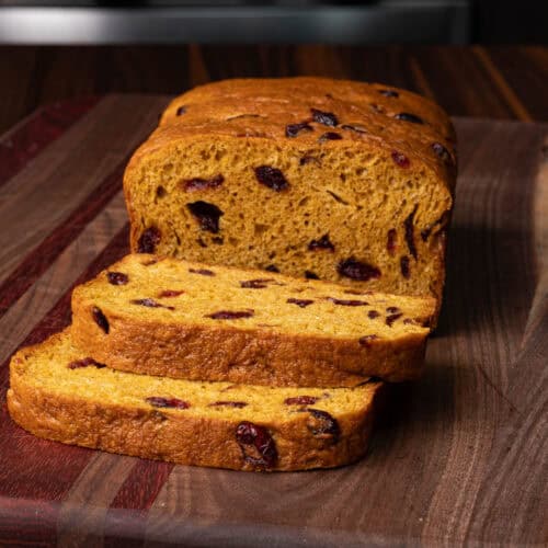 High protein orange cranberry loaf on a wooden cutting board.