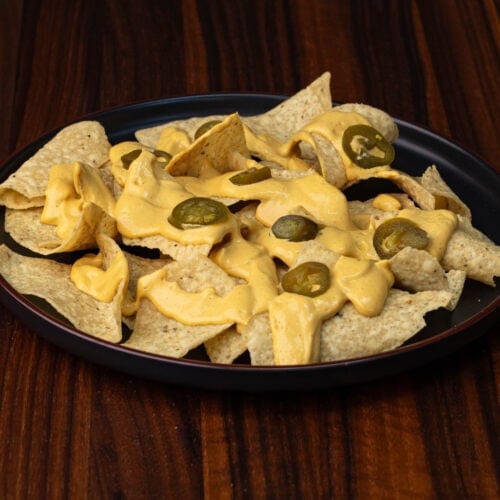 Vegan Nacho Cheese on top of tortilla chips with a few sliced jalapenos.