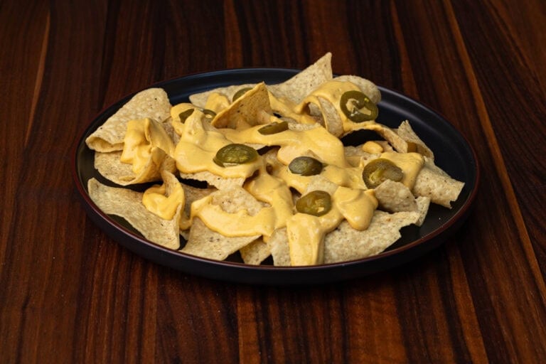 Vegan Nacho Cheese on top of tortilla chips with a few sliced jalapenos.