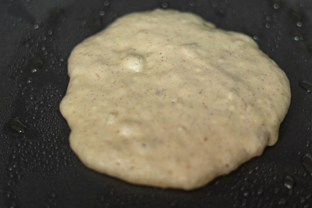A high protein banana pancake in a pan that needs to be flipped.