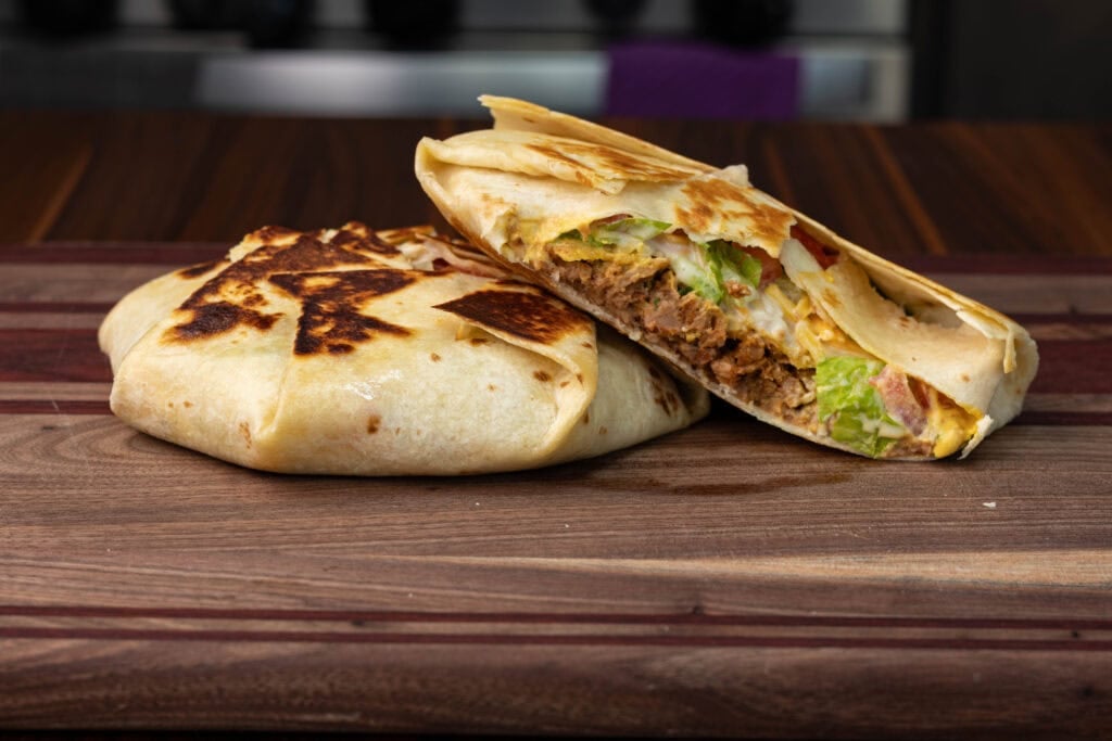 Two vegan TVP crunchwraps sitting on a wooden cutting board. One is cut open so you can see the inside.