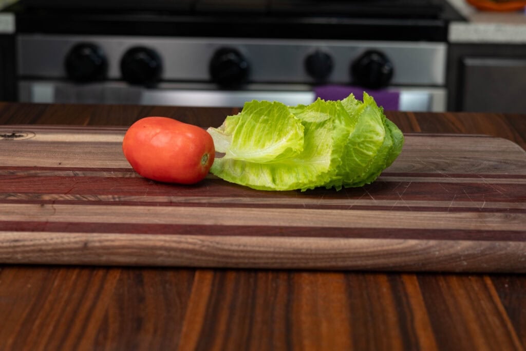 A tomato and lettuce on a wooden cutting board.