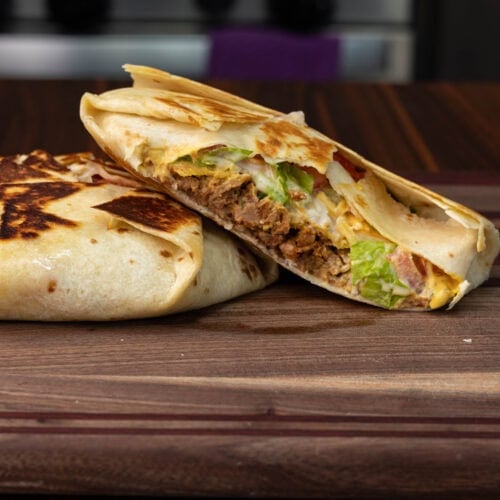 Two vegan TVP crunchwraps sitting on a wooden cutting board. One is cut open so you can see the inside.